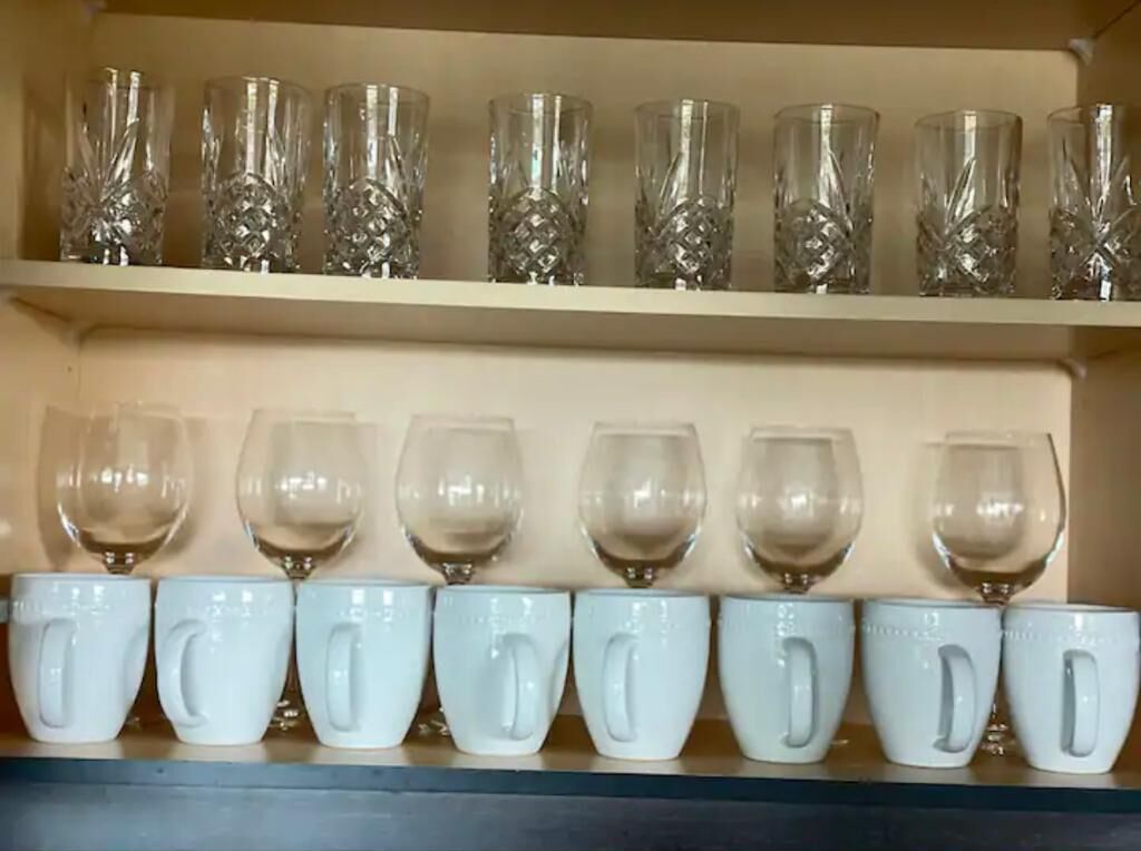 A shelf with rows of clear glassware and white ceramic mugs.