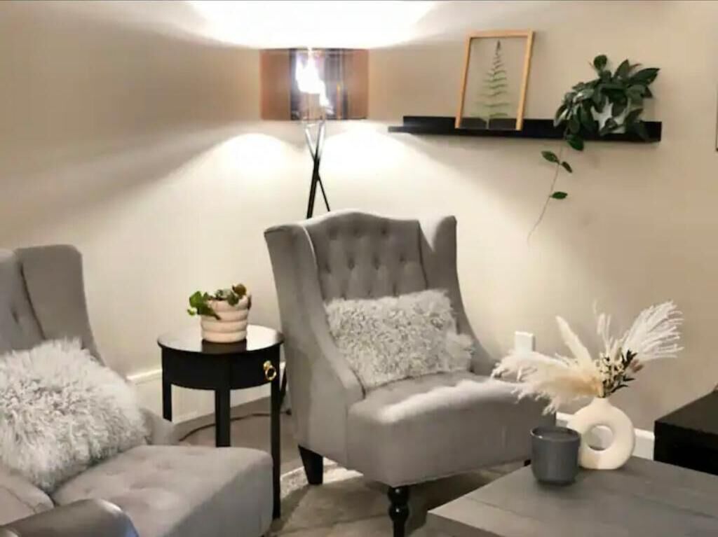 Una sala moderna con un sillón gris, una mesita auxiliar con una planta y un jarrón decorativo.