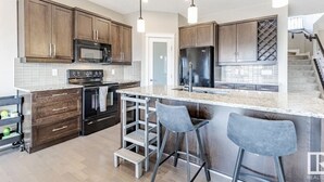 A modern kitchen with wooden cabinets, stainless steel appliances, and a bar area with stools. - Best home with lakeview access peace and quite place for family (Edmonton)