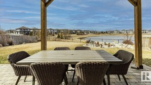 A covered patio with a table and chairs, overlooking a lake and residential area. - Best home with lakeview access peace and quite place for family (Edmonton)