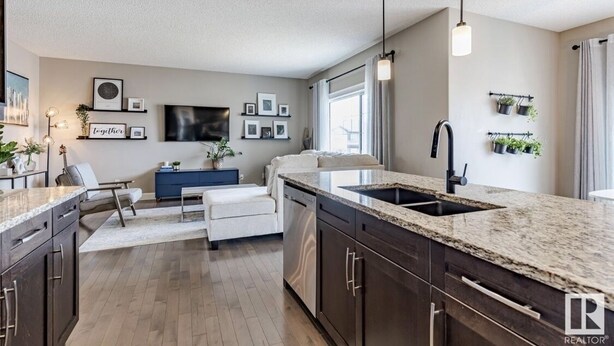A modern kitchen with dark wood cabinets, a granite countertop, and a built-in sink. - Best home with lakeview access peace and quite place for family (Edmonton)