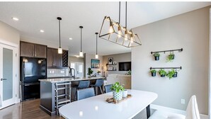 A modern kitchen with a central island, pendant lighting, and a dining area with a white table. - Best home with lakeview access peace and quite place for family (Edmonton)