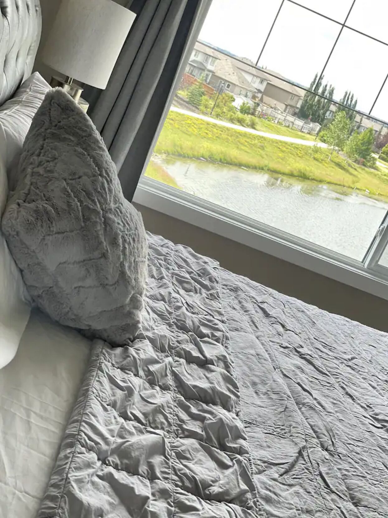 Un dormitorio con un ventanal grande, una cama con edredón gris y una almohada.