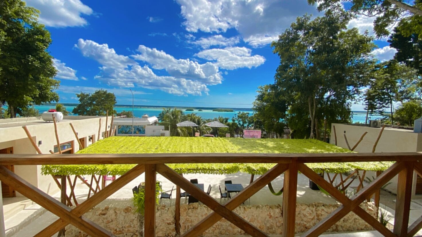A beachside view with a wooden deck, outdoor seating, and a clear view of the turquoise sea and sky.