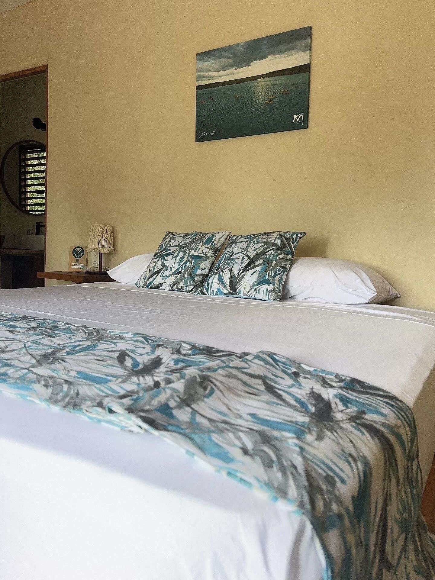 Un dormitorio con cama, un cuadro de una escena costera y una ventana con persianas.