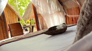 A cozy room with a bed, a wicker chair, and a view of a thatched-roof structure outside. - Hotel y Eco-Cabañas Azul María Bacalar (Bacalar)