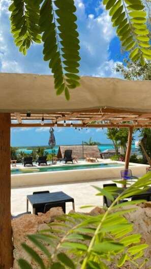 A covered outdoor seating area with a pool and lounge chairs, overlooking a clear blue sky and ocean. - Hotel y Eco-Cabañas Azul María Bacalar (Bacalar)