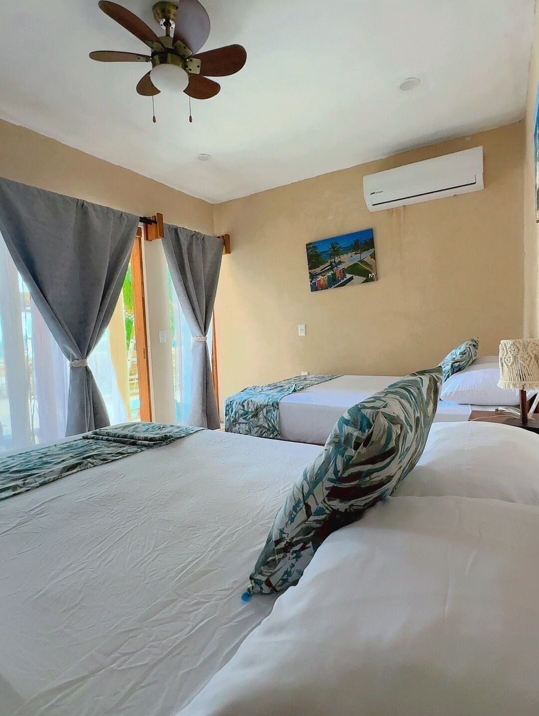 A hotel room with two beds, a ceiling fan, an air conditioning unit, and a painting on the wall.