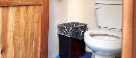 A small bathroom with a wooden door, a toilet, and a trash bin.