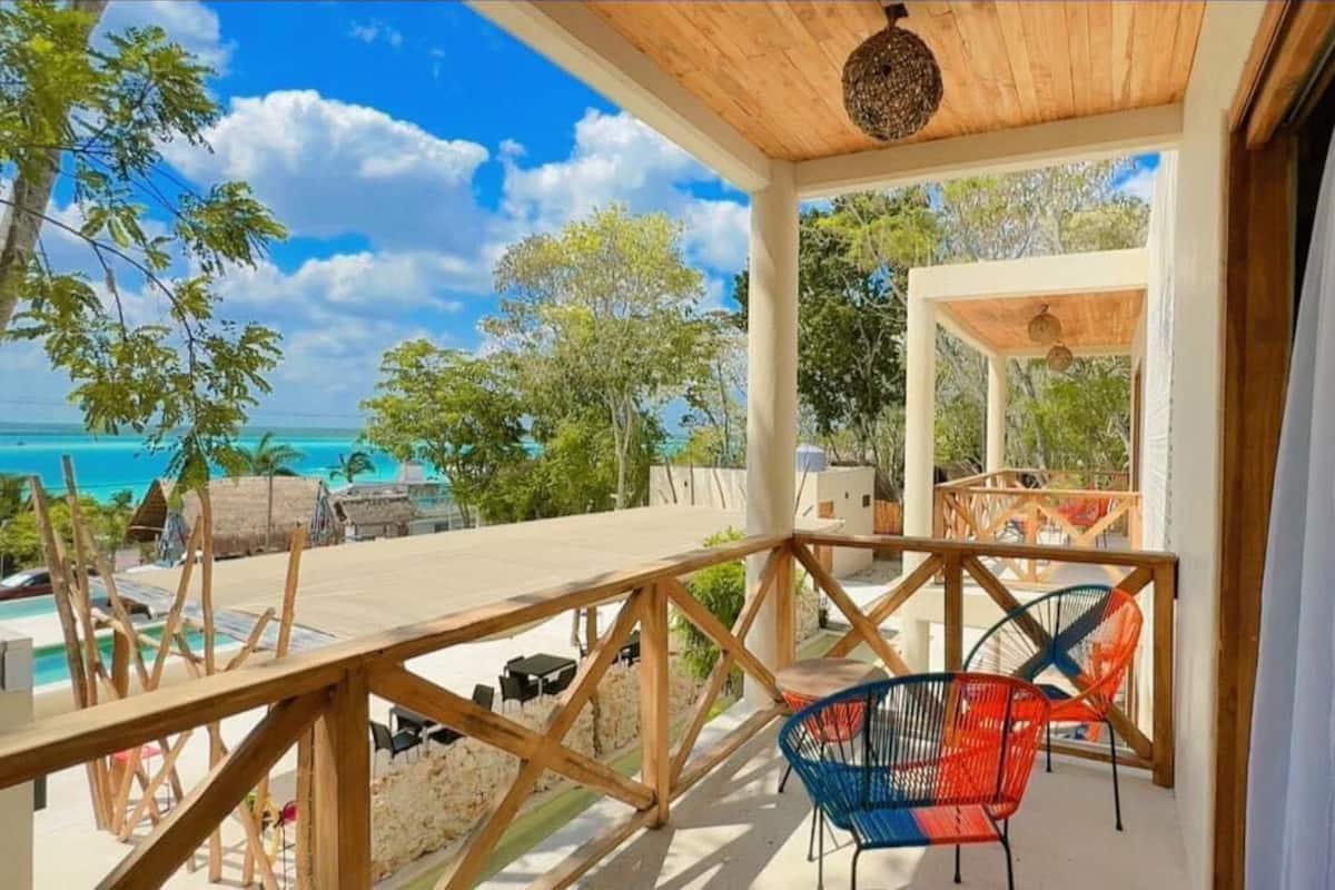 Eine Holzterrasse mit Pool, Stühlen und Blick aufs Meer.