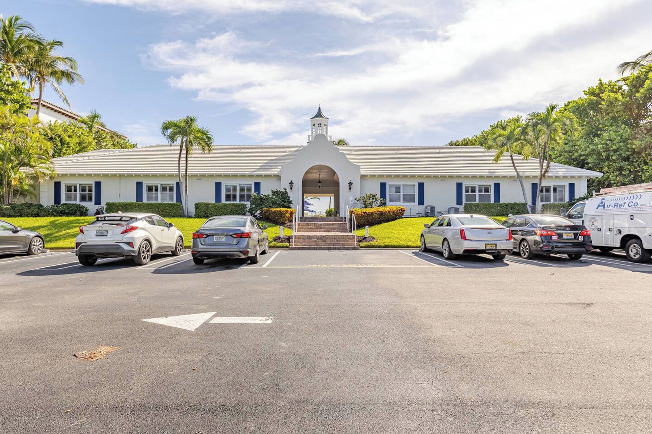 Un edificio con entrada principal, estacionamiento y varios automóviles estacionados.