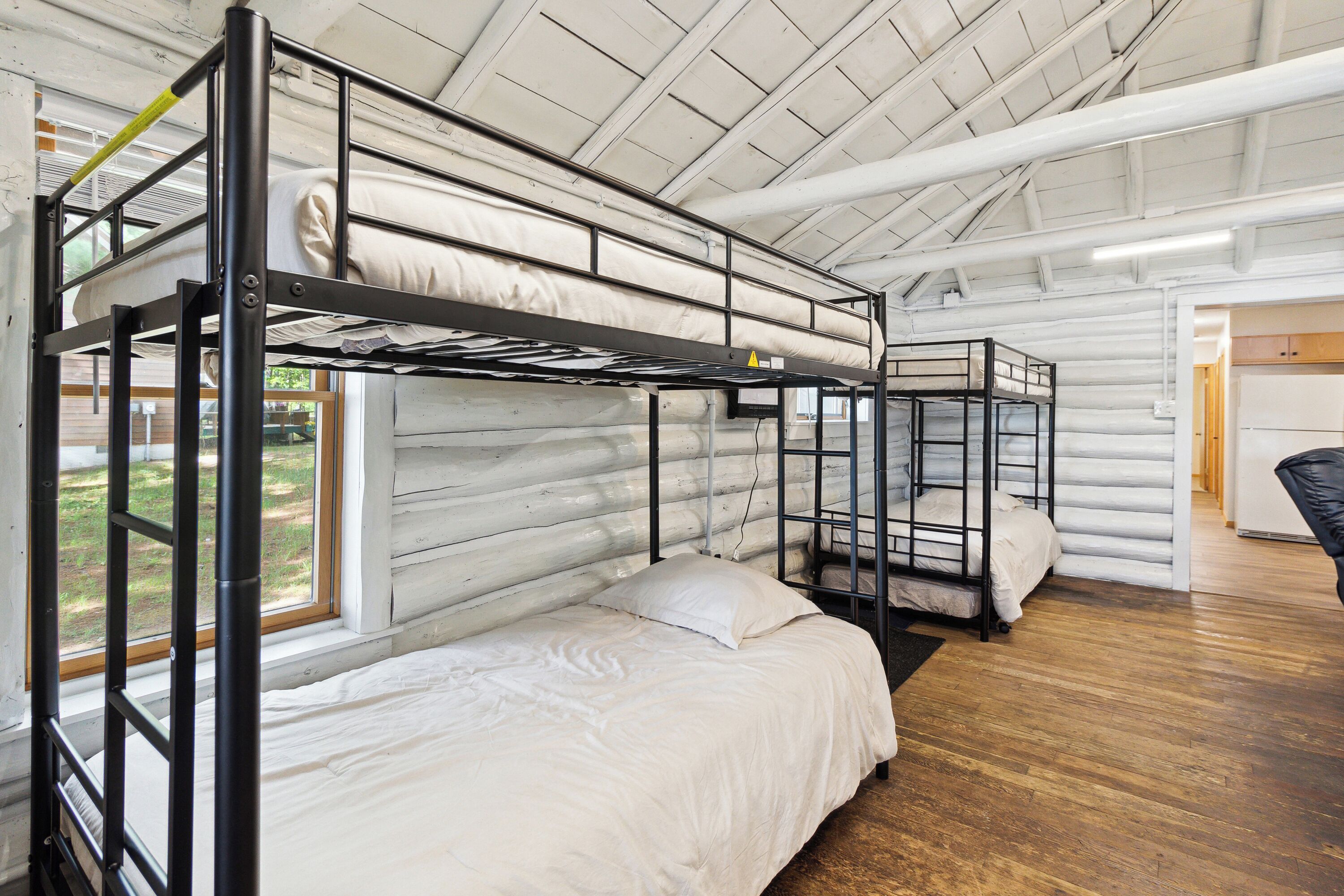 A bunk bed room with a wooden floor, a window, and a door.