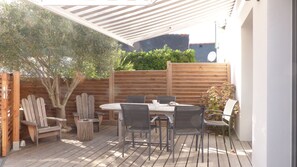 An outdoor patio with a wooden table and chairs, a wooden fence, and a tree.