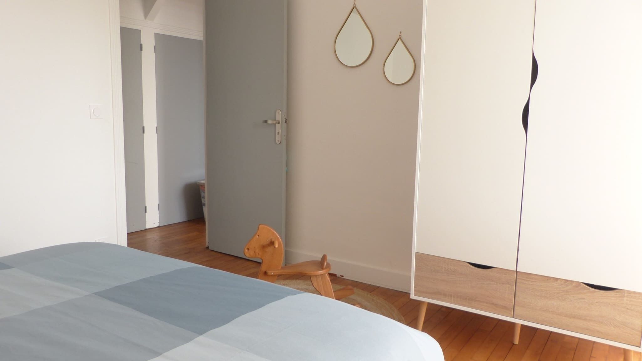 Une chambre à coucher avec un lit, un plancher en bois, une armoire blanche et une porte donnant sur une autre pièce.