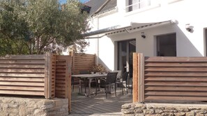 A patio with a table and chairs, a wooden fence, and a white building with a door and windows.
