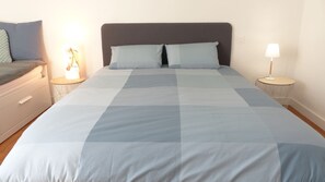 A neatly made bed with a checkered bedspread, two bedside tables with lamps, and a nightstand with a lamp.