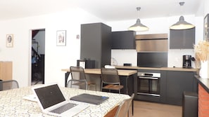 Une cuisine moderne avec des meubles noirs, des appareils en acier inoxydable et un coin repas où se trouve un ordinateur portable sur la table.