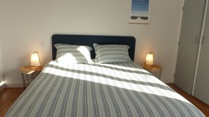 Una cama con ropa de cama a rayas, dos lámparas de noche y un cuadro en la pared.