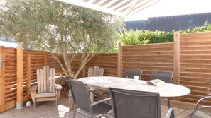 An outdoor patio with a round table and chairs, surrounded by wooden fences and a tree.
