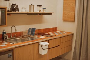 Une petite cuisine équipée d’un évier, d’un égouttoir, d’une machine à café et d’une étagère avec des bocaux et un grille-pain.