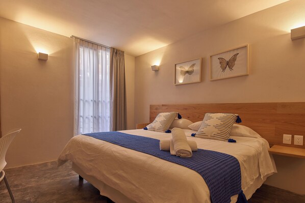 Une chambre d’hôtel avec un grand lit, une table de chevet, une chaise et une fenêtre avec des rideaux.