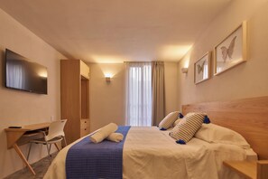 Une chambre d’hôtel avec un lit, un bureau, une chaise, une télévision et une fenêtre avec des rideaux.