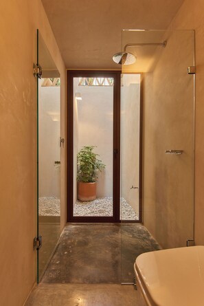 Une salle de bain moderne avec une porte en verre donnant accès à une zone de douche, une plante en pot et une baignoire.