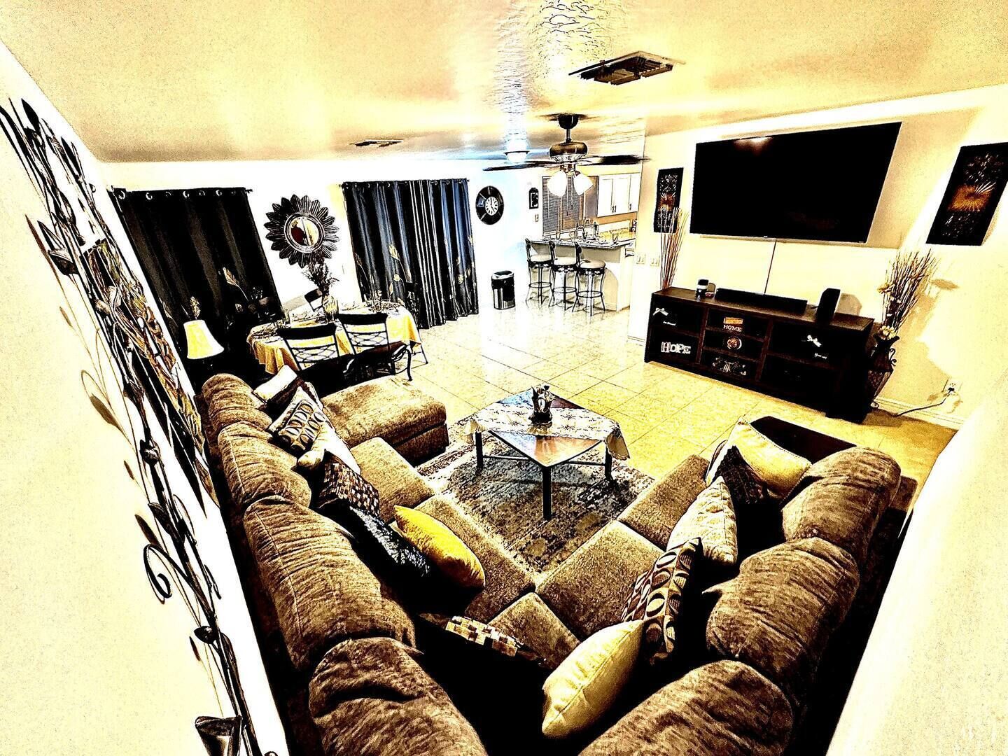 A living room with a large sectional sofa, a coffee table, and a TV mounted on the wall.