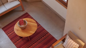 Et værelse med et træbord, en flettet kurv, et mønstret tæppe, en sofa og en stol med pude.