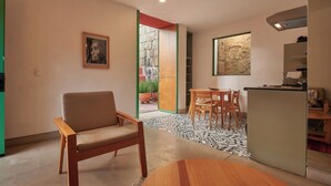 A modern living room with a sofa, a dining table with chairs, a kitchen area with a refrigerator, and a view of the outside.