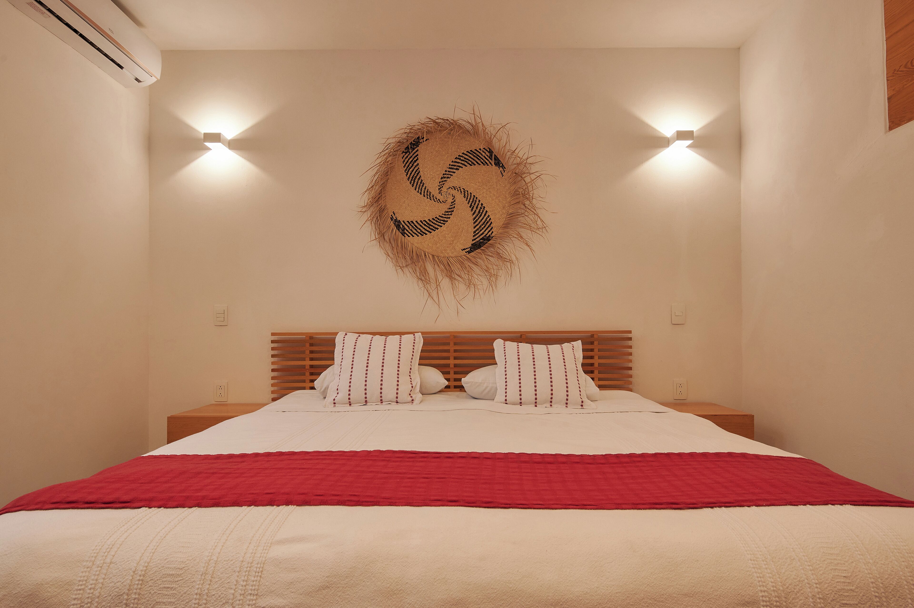 Una camera da letto con un letto, una coperta rossa, un poggiatesta in legno e un punto luce a parete.