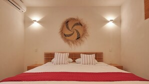 A bedroom with a bed, a red blanket, a wooden headboard, and a wall-mounted light fixture.