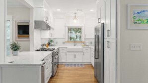 A modern kitchen with white cabinetry, a stainless steel range hood, a built-in oven, and a refrigerator.