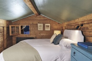 Ein Schlafzimmer einer Holzhütte mit einem Bett, Kissen, einem Schminktisch und gerahmten Bildern an der Wand.