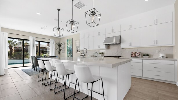 Een moderne keuken met witte kasten, een centraal eiland met barkrukken, hanglampen en uitzicht op de omgeving.