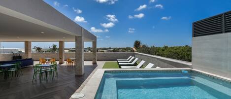 A rooftop pool area with a clear view of the sky, a pool, lounge chairs, and outdoor seating.