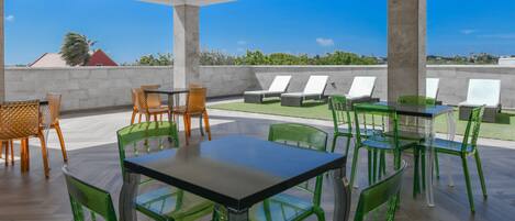 A rooftop terrace with a table and chairs, lounge chairs, and a view of the landscape.