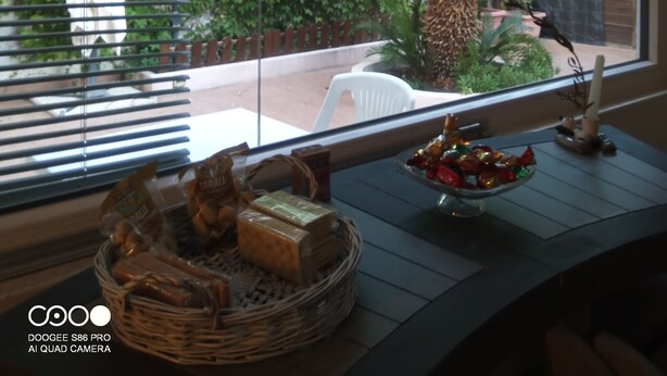 Ein Zimmer mit einem großen Fenster mit Blick auf einen Garten, ein Korbwäsche mit Snacks und ein kleiner Tisch mit einer Kerze und Dekoration.