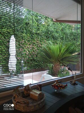 A room with a large window overlooking a garden, a wicker basket with snacks, and a small table with a candle and decorative items.