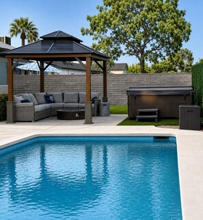 A swimming pool with a built-in hot tub, a covered seating area, and a patio with a sofa and outdoor furniture.