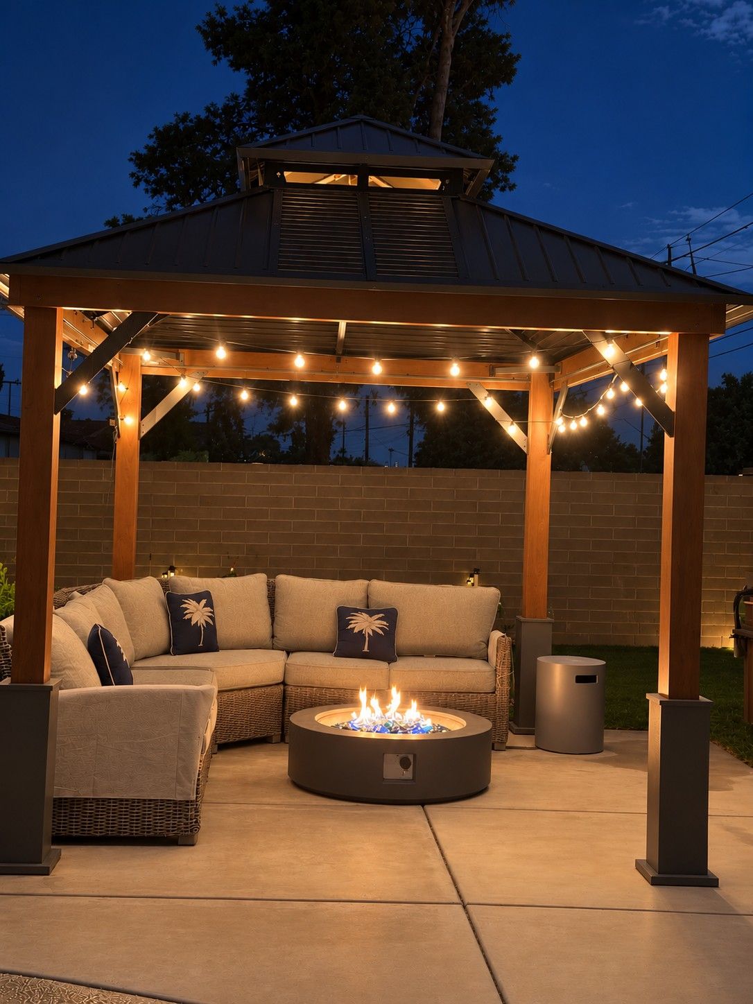 A covered outdoor seating area with a fire pit, string lights, and a brick wall in the background.