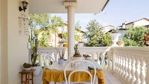 A balcony with a table and chairs, potted plants, and a view of buildings and trees. - Alexander's Home (Collecorvino)