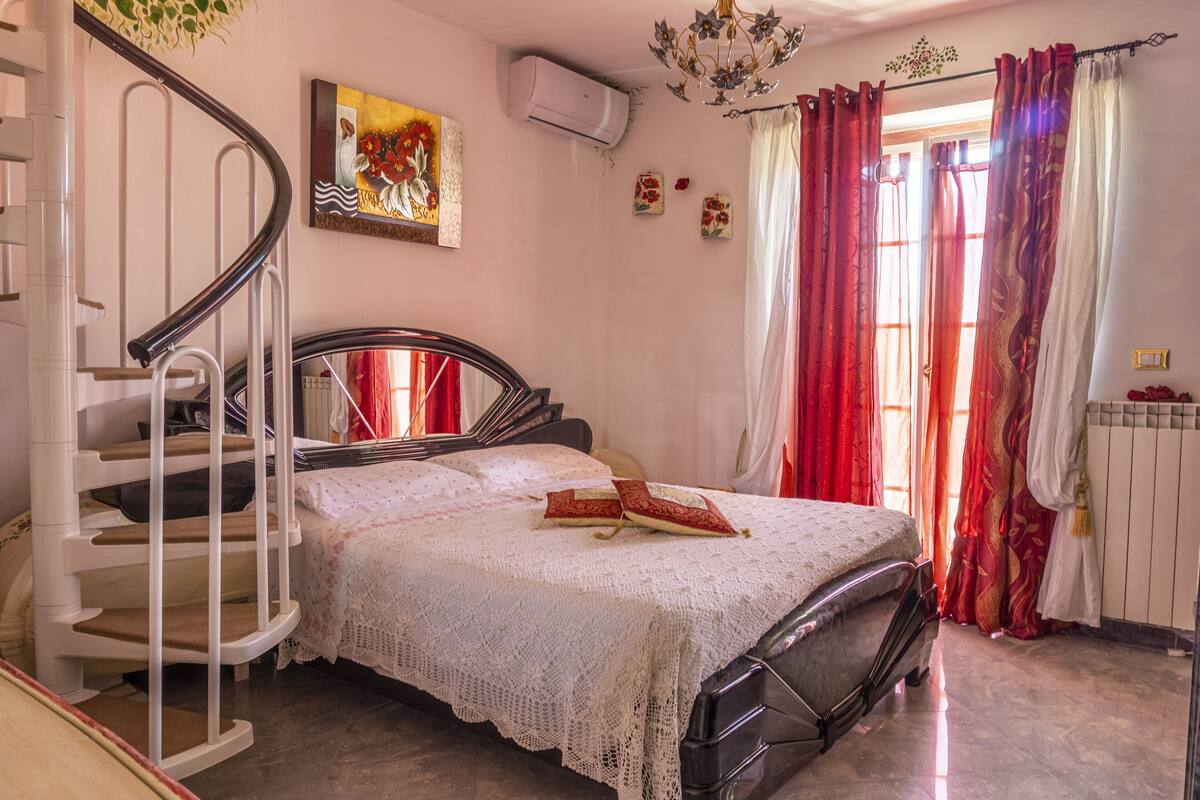 A bedroom with a bed, a staircase, a radiator, and a window with curtains.