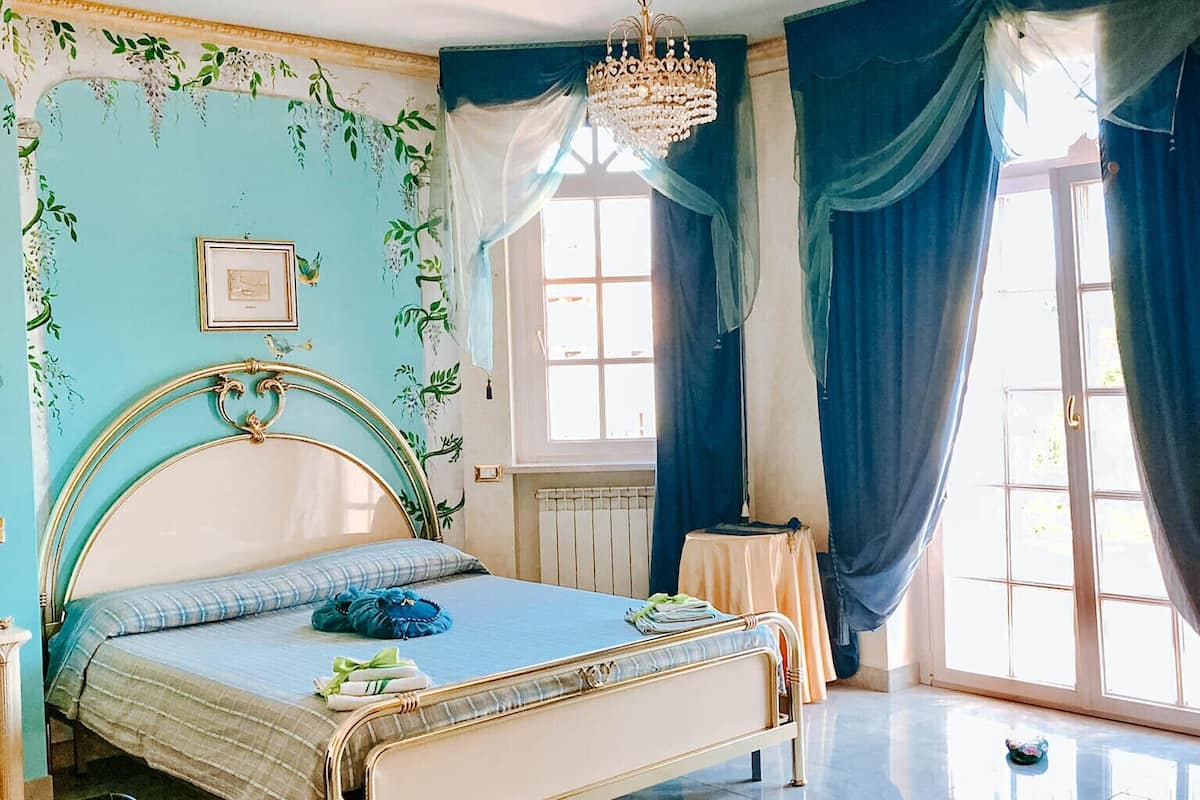 A bedroom with a bed, a chandelier, a window with curtains, and a radiator.