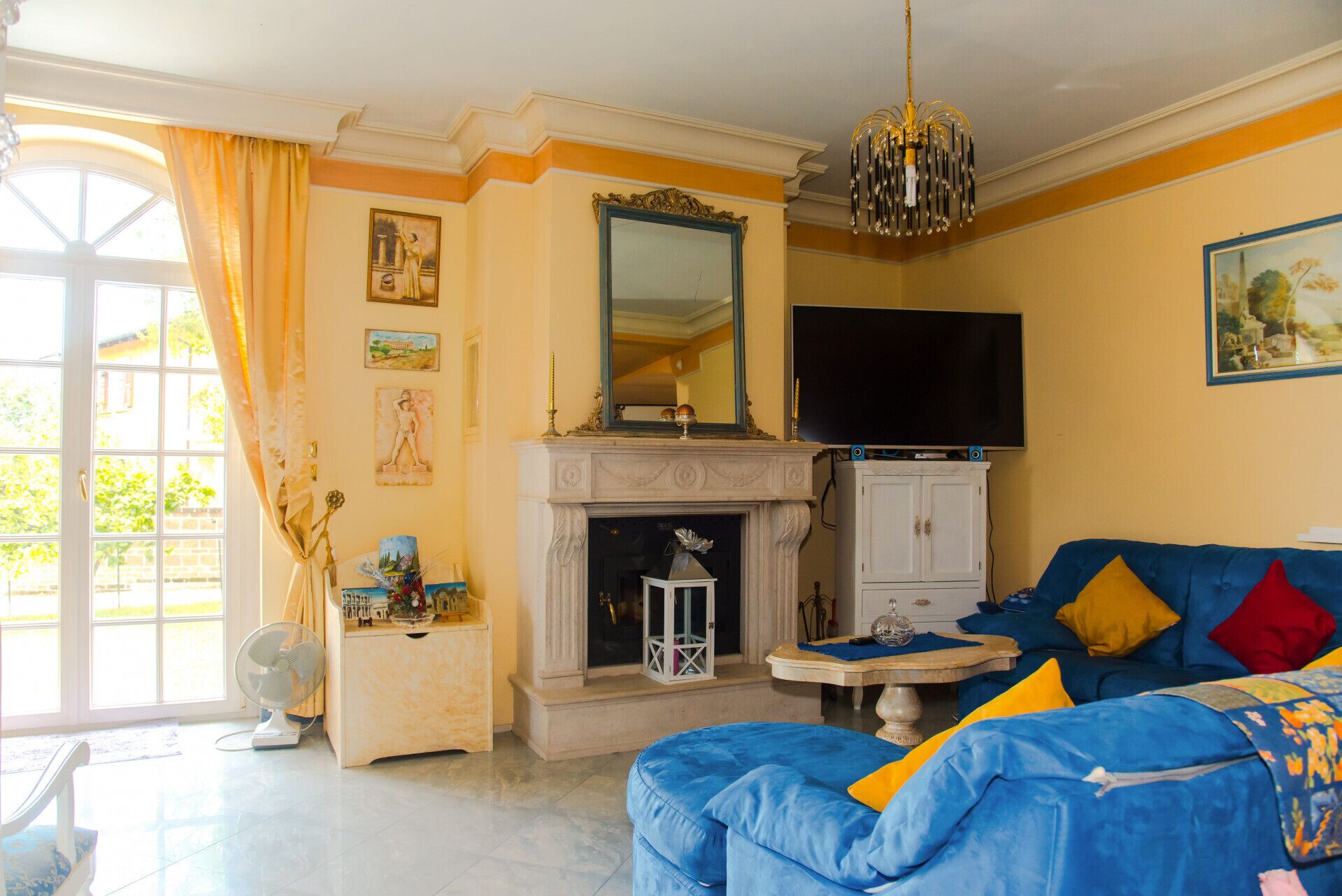 Un salon avec une cheminée, un téléviseur et un canapé bleu agrémenté de coussins colorés.