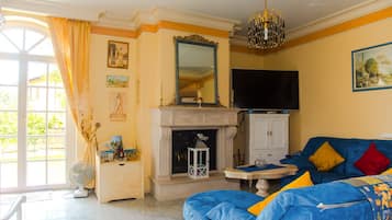 Una sala de estar con chimenea, televisor y sofá azul con cojines de colores.