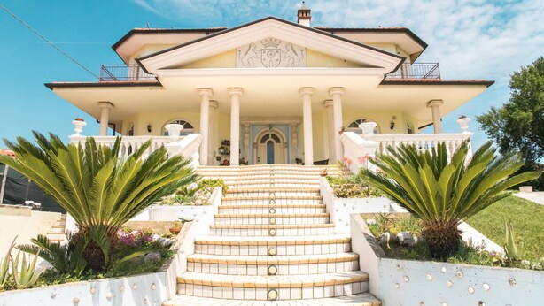 A grand building with a symmetrical facade, large columns, and a central entrance with a decorative arch. - Alexander's Home (Collecorvino)