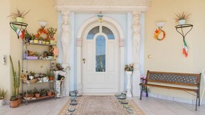 A well-lit entrance with a white door, a bench, and potted plants on either side. - Alexander's Home (Collecorvino)