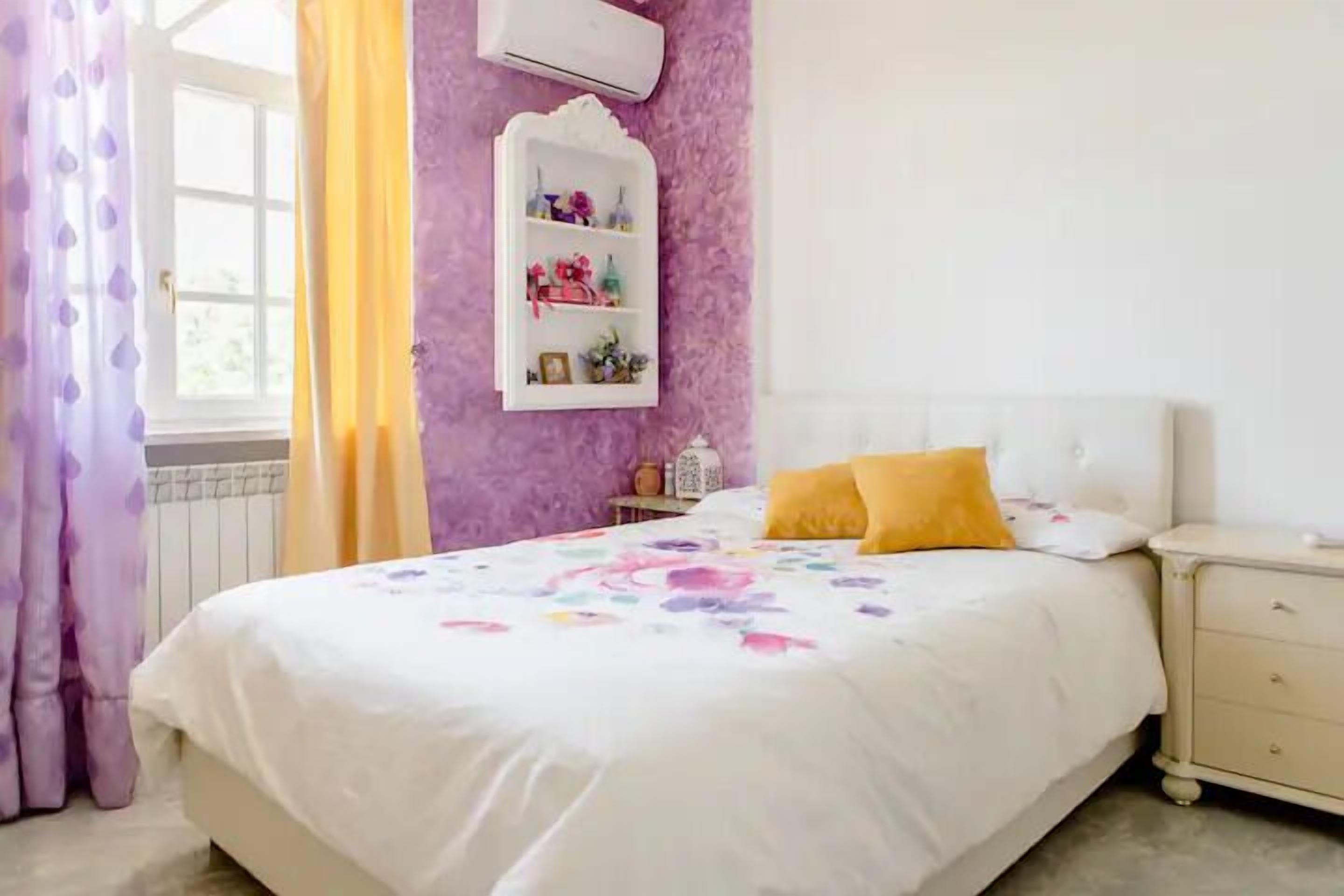 Une chambre à coucher comprenant un lit, une table de chevet, une étagère avec des objets décoratifs et une fenêtre avec des rideaux.