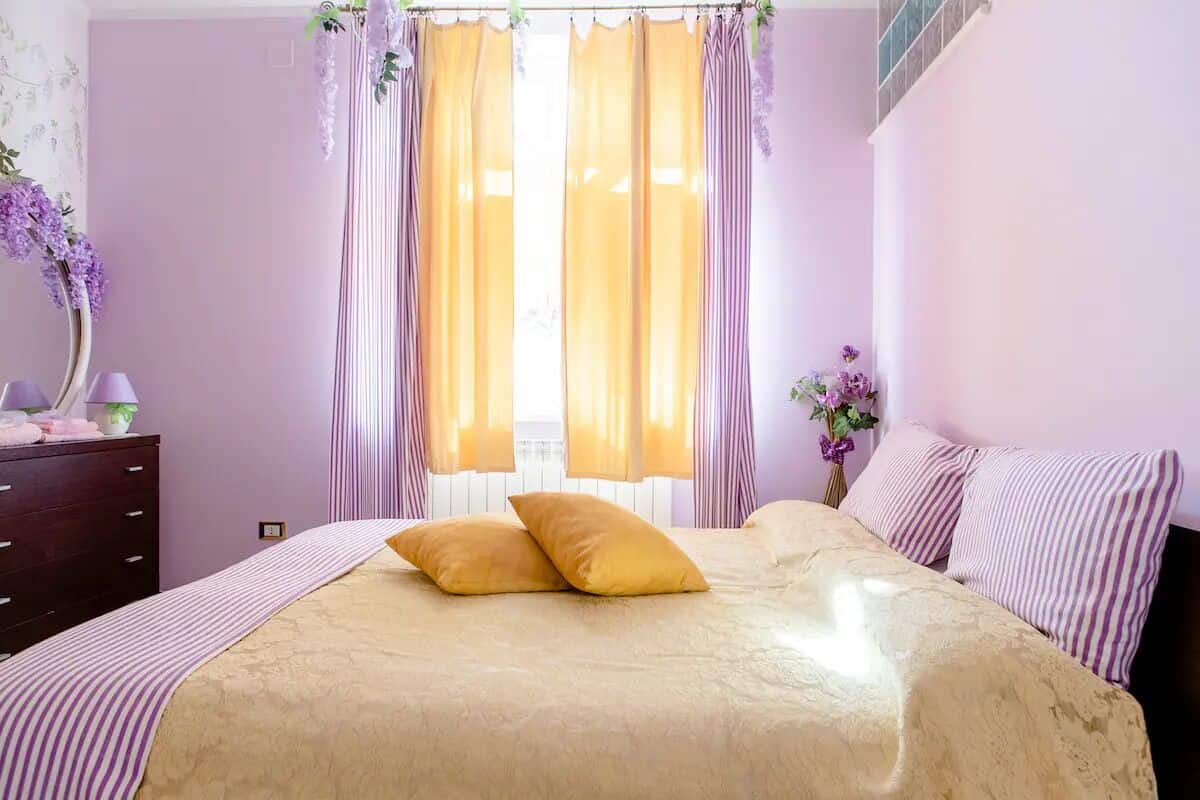 A bedroom with a bed, a dresser, and a window with curtains.